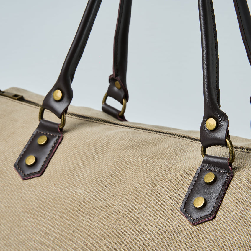 Beige duffel bag with black straps on a light gray background
