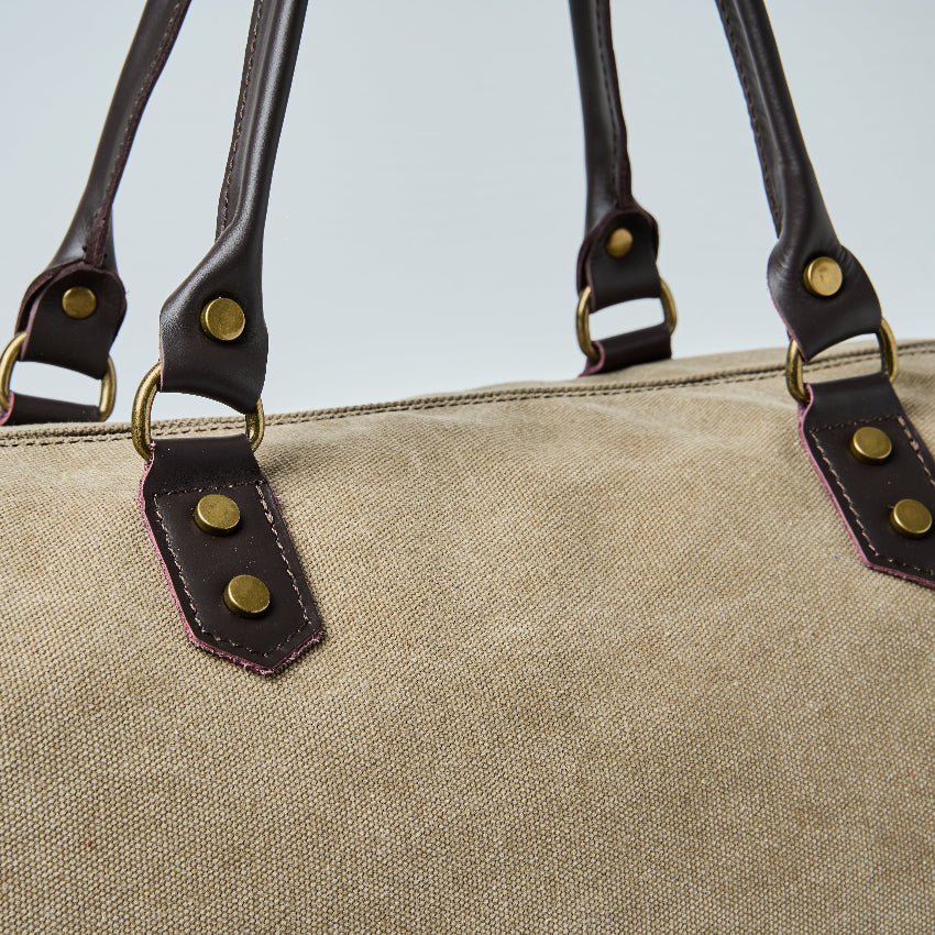 Beige duffel bag with black straps on a light gray background
