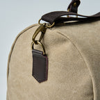 Beige duffel bag with black straps on a light gray background