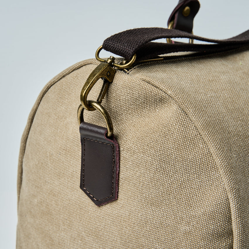 Beige duffel bag with black straps on a light gray background