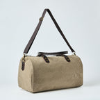Beige duffel bag with black straps on a light gray background